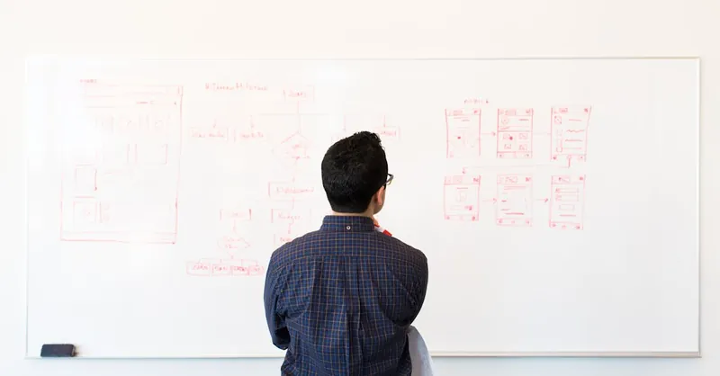 Man standing at a whiteboard planning UX design concepts in a modern office setting.