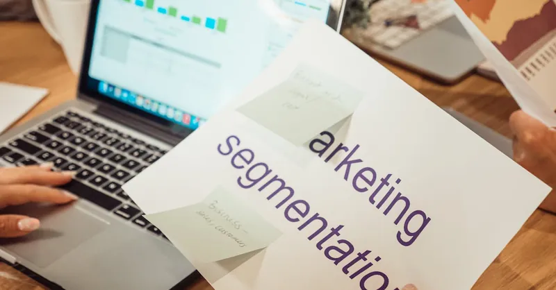A modern workspace showing hands analyzing marketing data on a laptop and paper documents.