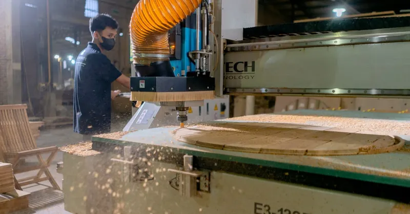 A carpenter operates a CNC machine in a factory, showcasing modern woodworking technology.