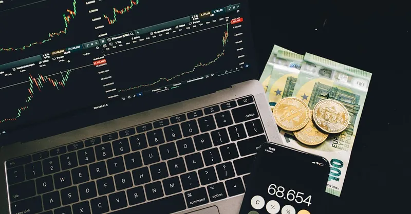 A laptop displaying stock charts with Bitcoin, Euros, and a cellphone calculator, showcasing financial analysis.