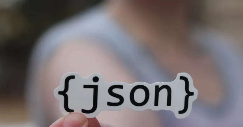 A hand holding a JSON text sticker, symbolic for software development.