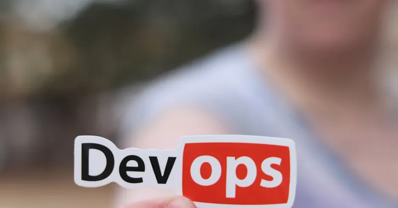 A close-up image featuring a DevOps sticker held by a person outdoors.