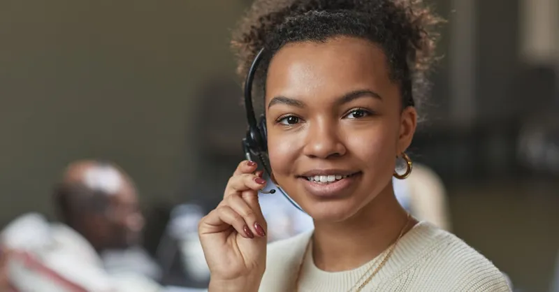 Friendly woman in a call center environment, wearing a headset and smiling.