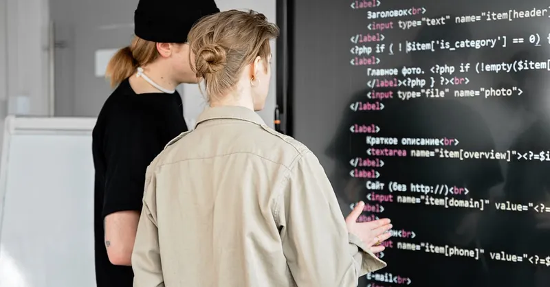 Two developers examining code on a large screen in a modern office space, focusing on web development.