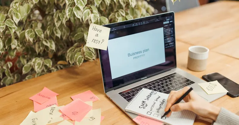A workspace with a laptop, sticky notes, and a notepad for business planning.