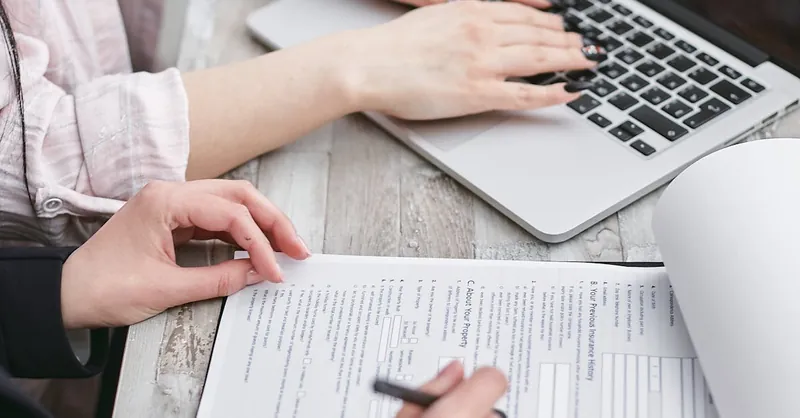 Close-up of hands typing on a laptop and reviewing business documents, focused on finance and legal tasks.