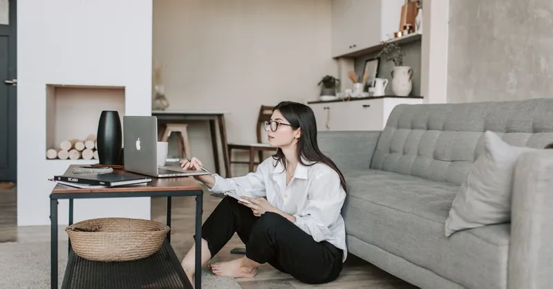 Asian woman working on laptop from cozy living room, showcasing modern home office setup.