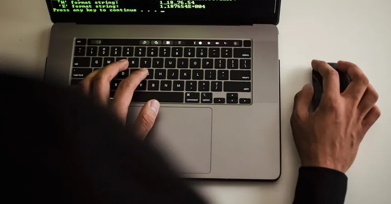 Close-up of a programmer typing on a laptop, displaying code on the screen.