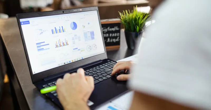Focused business analysis with charts and graphs on a laptop in a modern office setting.