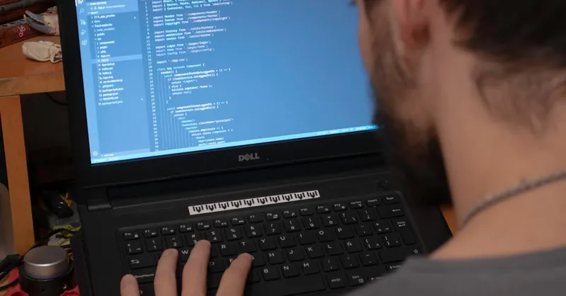Man working on code on a laptop in an office, showcasing modern remote work setup.