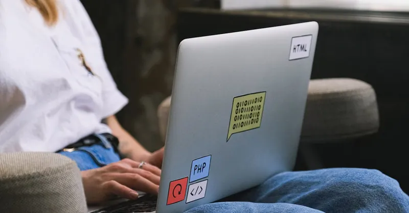 Person typing on a laptop with coding stickers, symbolizing remote work and freelancing.