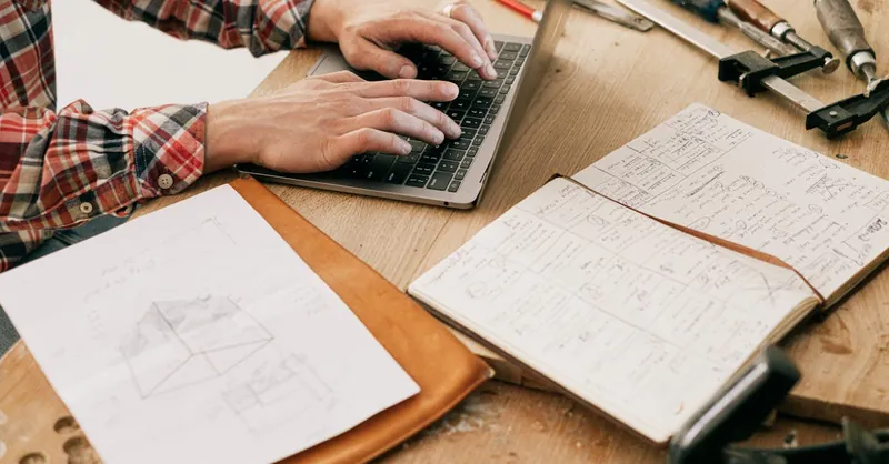 A woodworker uses a laptop to design furniture in a workshop setting, highlighting the blend of technology and craftsmanship.