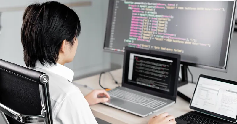 A software developer working on code with multiple screens in a modern office setting.