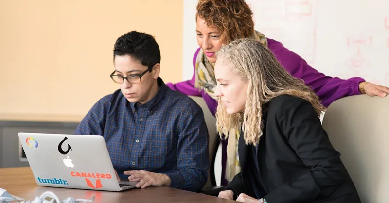 Team of three people collaborating on a laptop in an office setting.