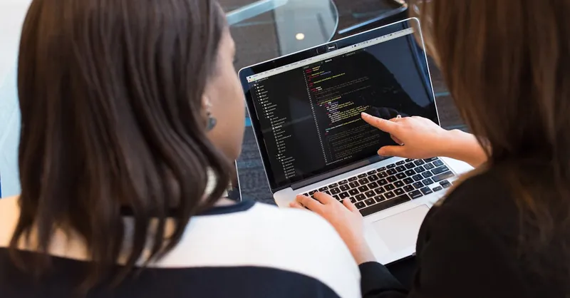 Two women working together on software programming indoors, focusing on code.