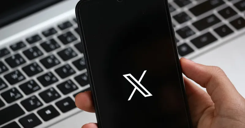 A hand holds a smartphone displaying a modern app interface, with a laptop keyboard in the background.