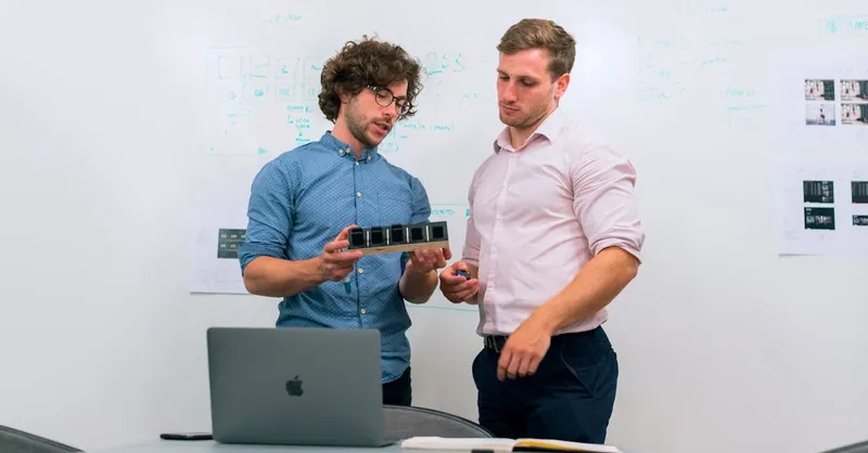 Two men in an office discussing and reviewing a tech prototype.